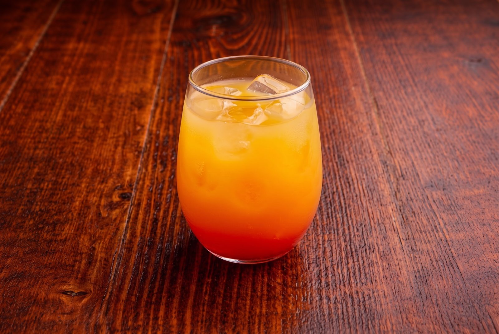 Orange and red layered drink with ice in a glass