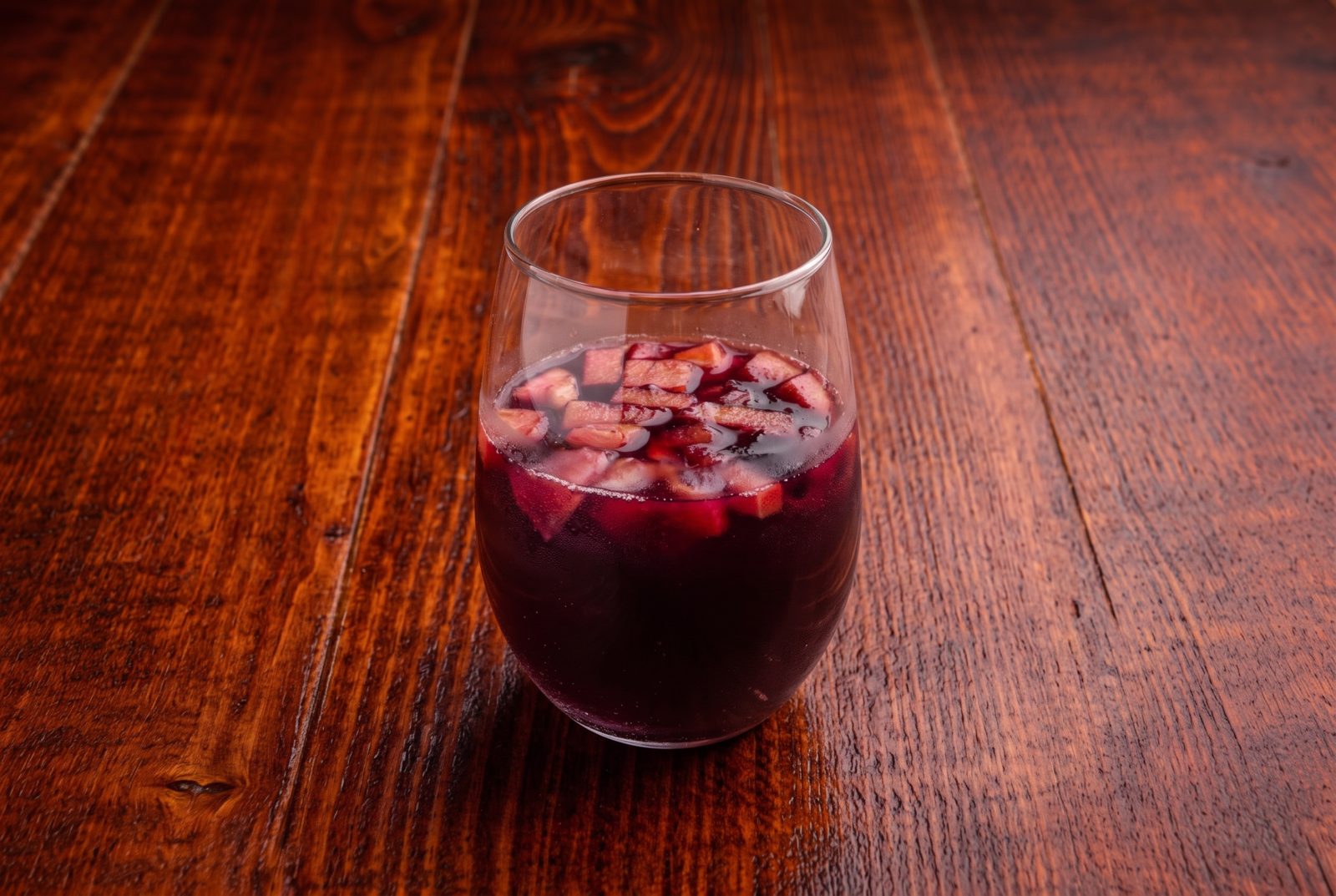 Glass of red sangria with diced fruit on a rustic wooden table
